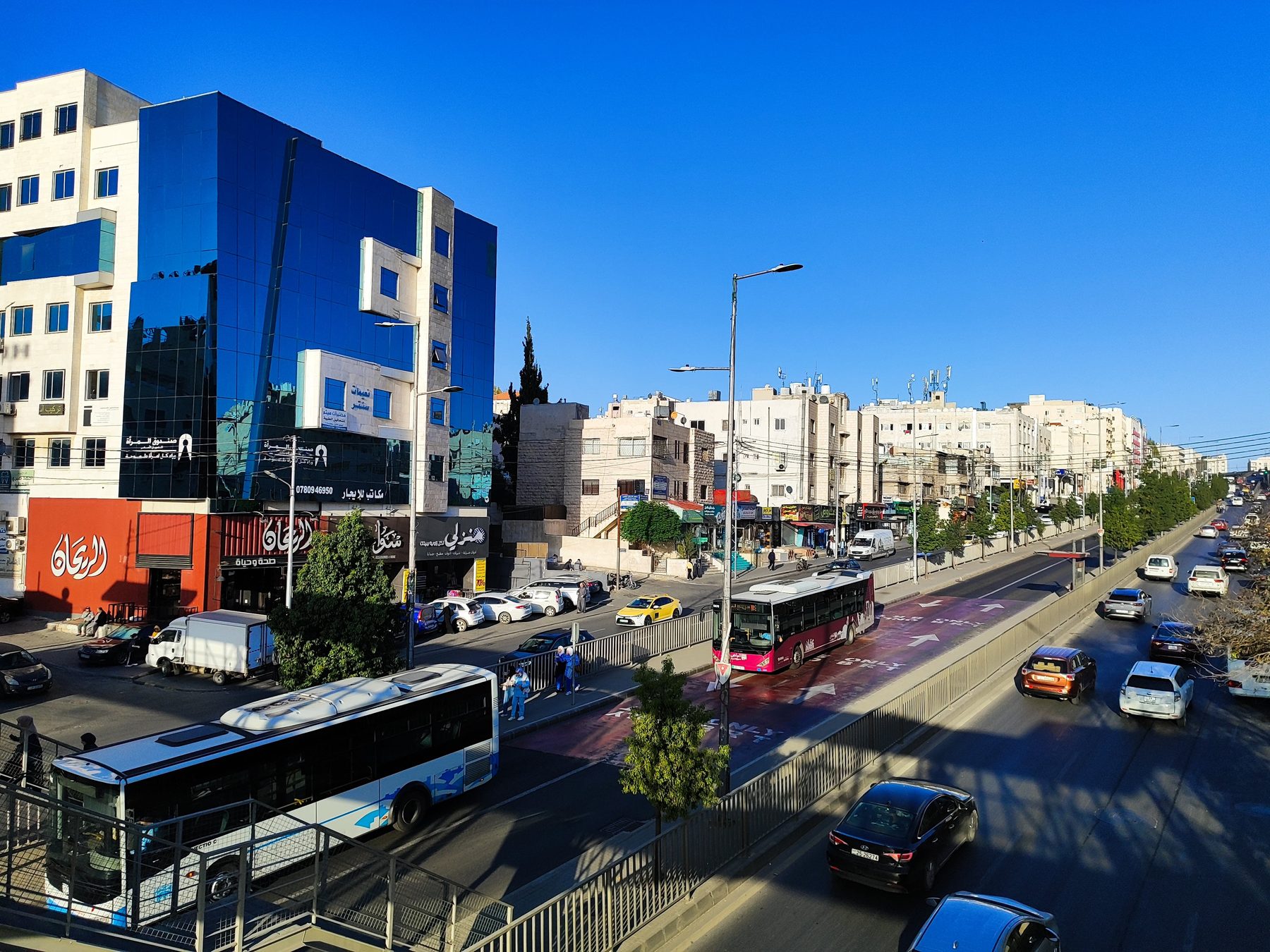 واجهة نعيمات سنتر الزجاجية الزرقاء على شارع الملكة رانيا في صويلح، ومحطة الباص السريع أمامها